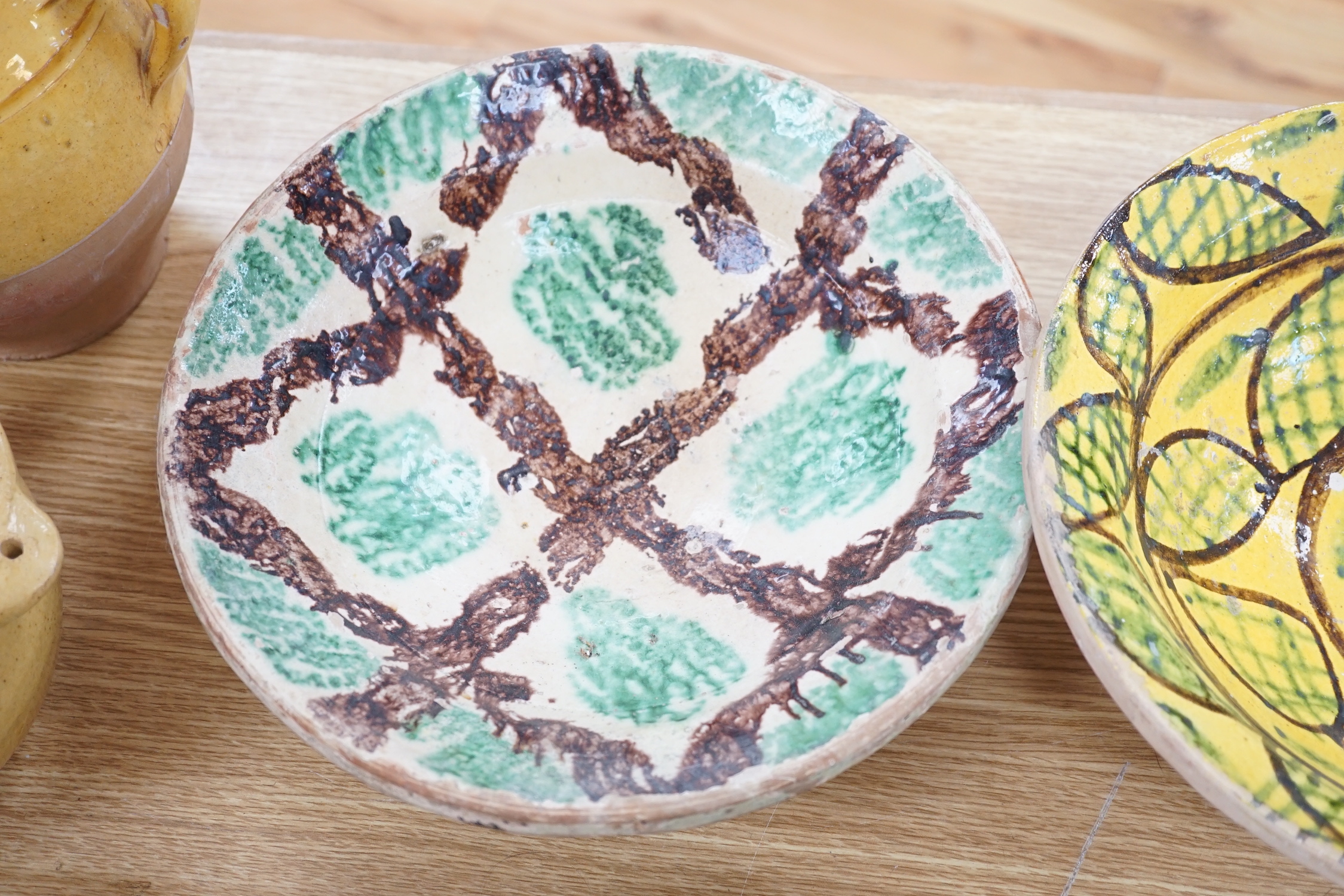 A group of Mediterranean slip decorated pottery dishes, a jar and cover and a bowl, predominantly with yellow and green grounds, the largest 26cm in diameter